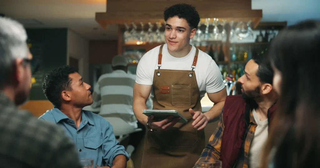 Jonge medewerker in de bediening neemt met een tablet de bestelling op aan een tafel in een café